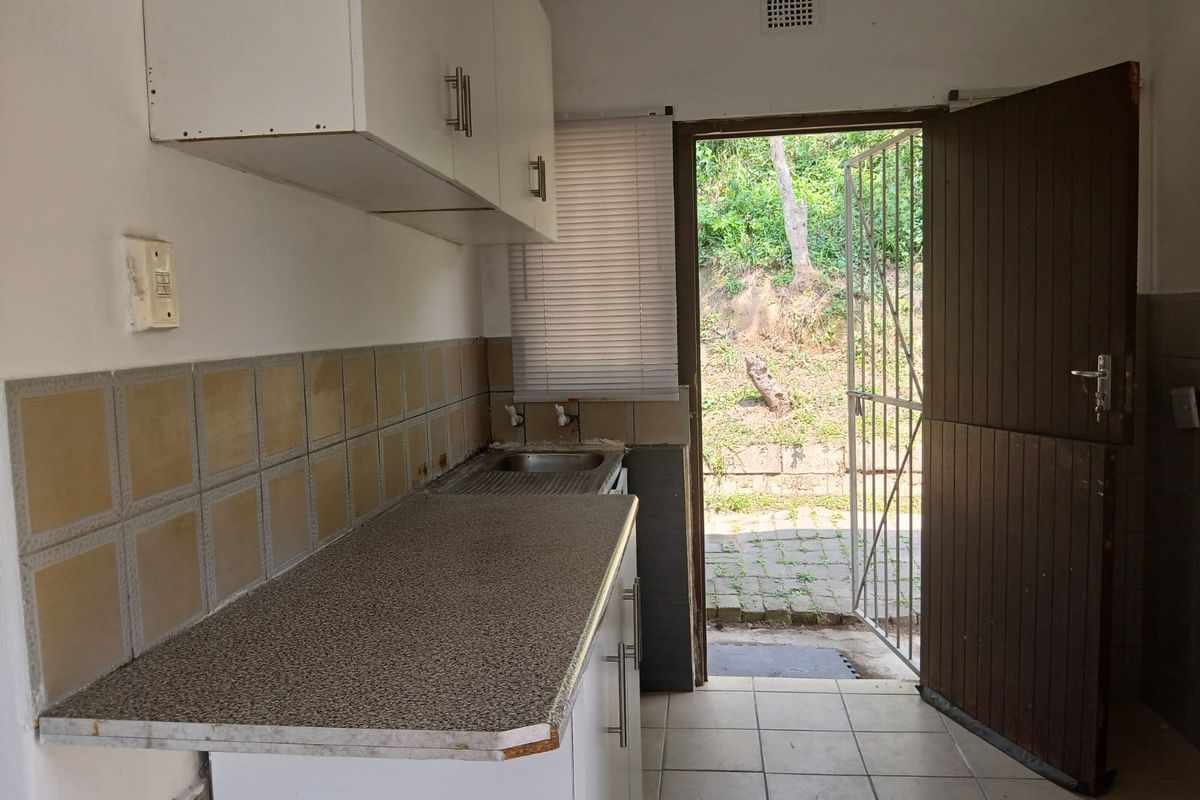 A compact kitchen area featuring built-in cabinetry, a laminate countertop, and a stainless steel sink, with direct access to an outdoor area.