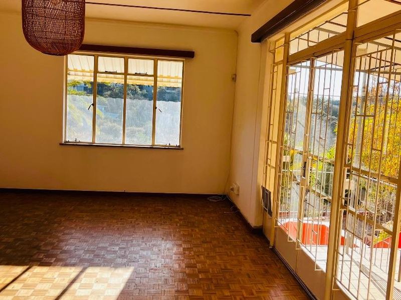 A bright, empty living room featuring original parquet flooring, large steel-framed windows, and glass doors leading to an outdoor area.