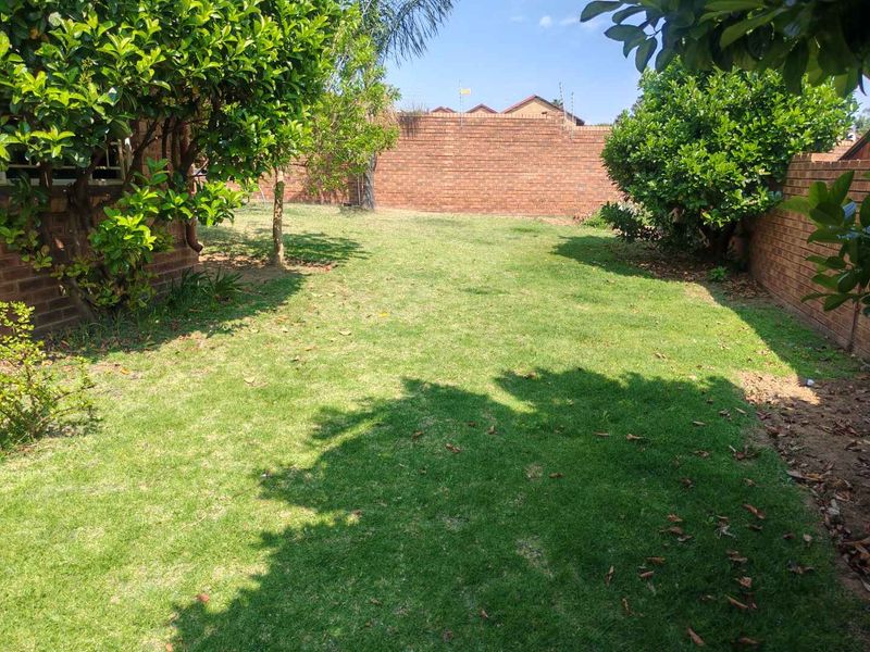 A private rear garden featuring a well-maintained lawn, established trees, and secure brick boundary walls with electric fencing.