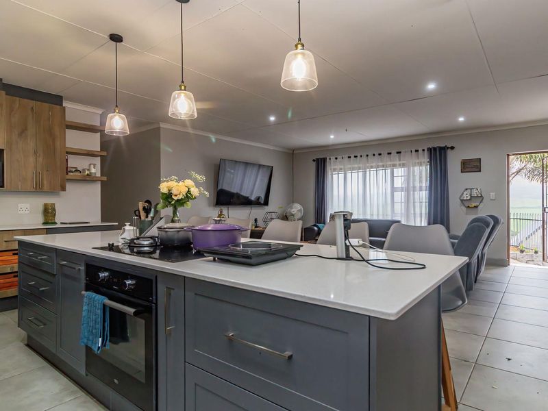 Modern open-plan kitchen and living area featuring a central island with built-in oven, sleek cabinetry, and tiled flooring throughout.