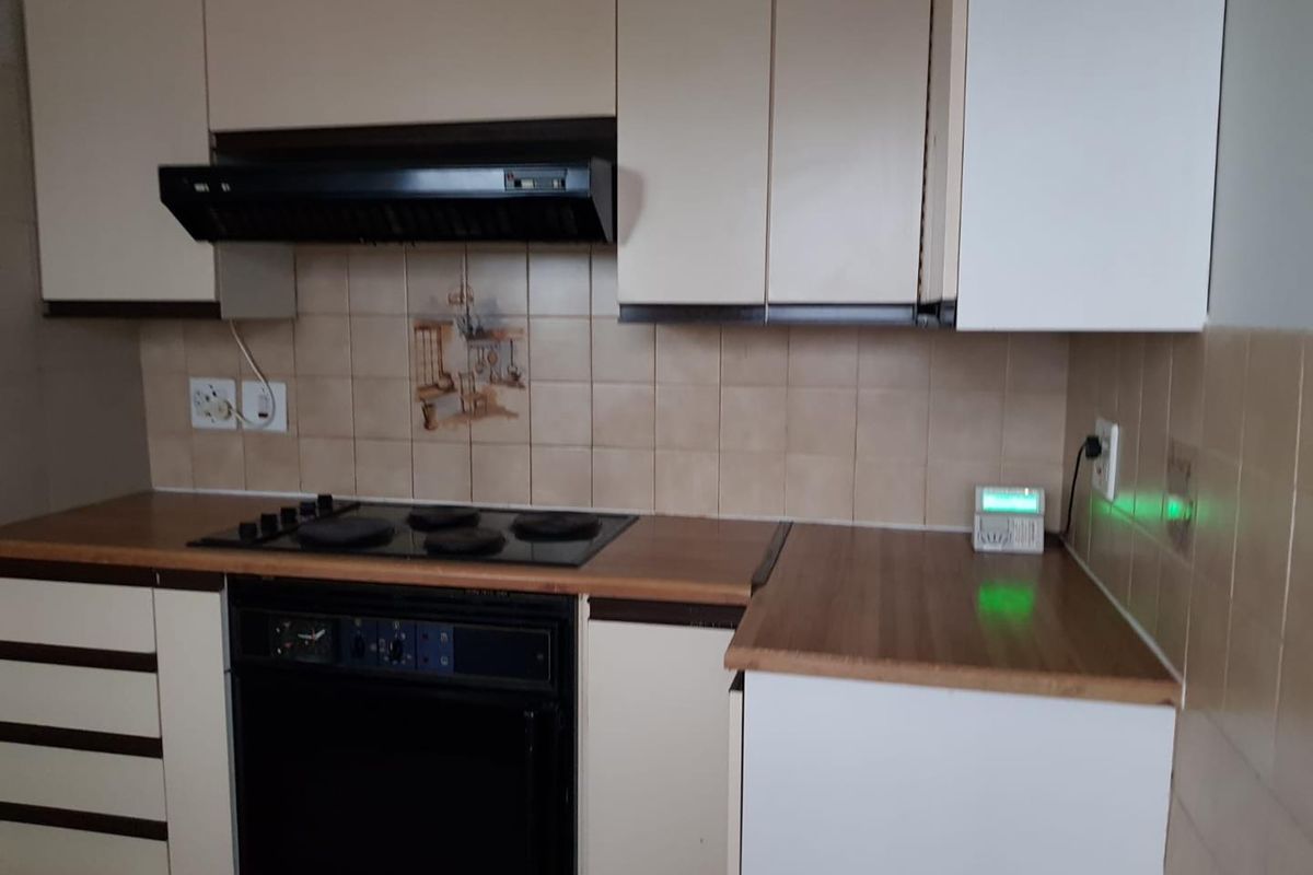 A functional kitchen featuring built-in cabinetry, laminate countertops, an integrated electric hob, oven, and extractor fan with a tiled backsplash.