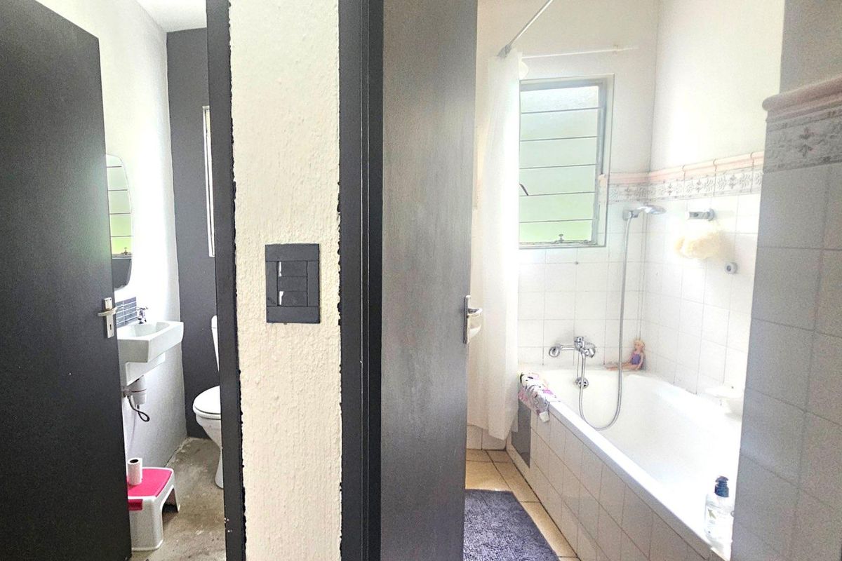 A functional bathroom featuring a bathtub with shower attachment, a wall-mounted basin, and a toilet, finished with classic white tiling.