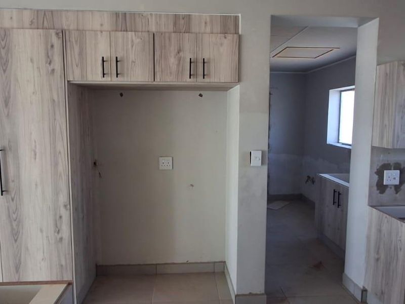 An unfinished kitchen space featuring light wood-grain cabinetry, tiled floors, and exposed wall sections awaiting final finishes and backsplash installation.
