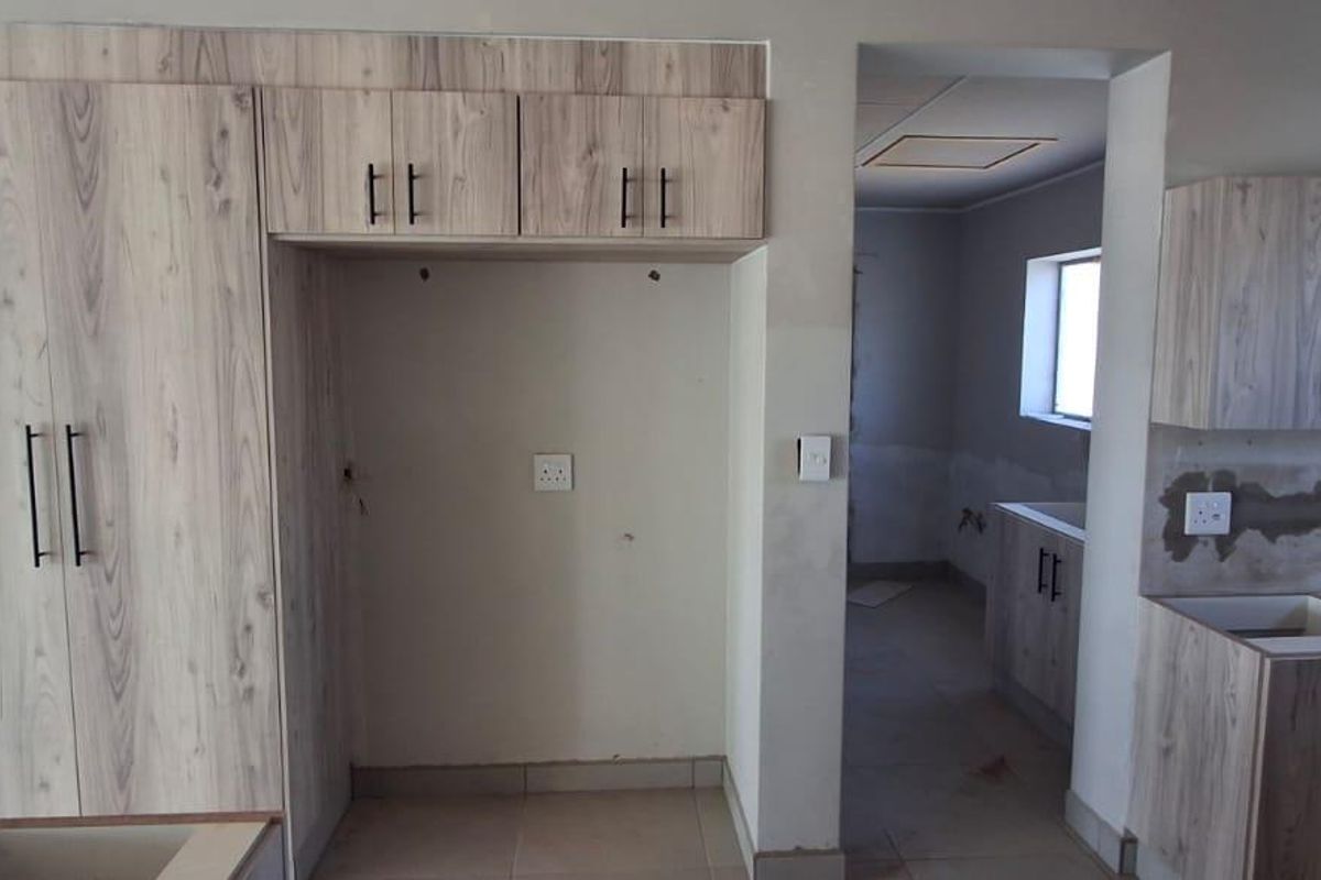 An unfinished kitchen space featuring light wood-grain cabinetry, tiled floors, and exposed wall sections awaiting final finishes and backsplash installation.