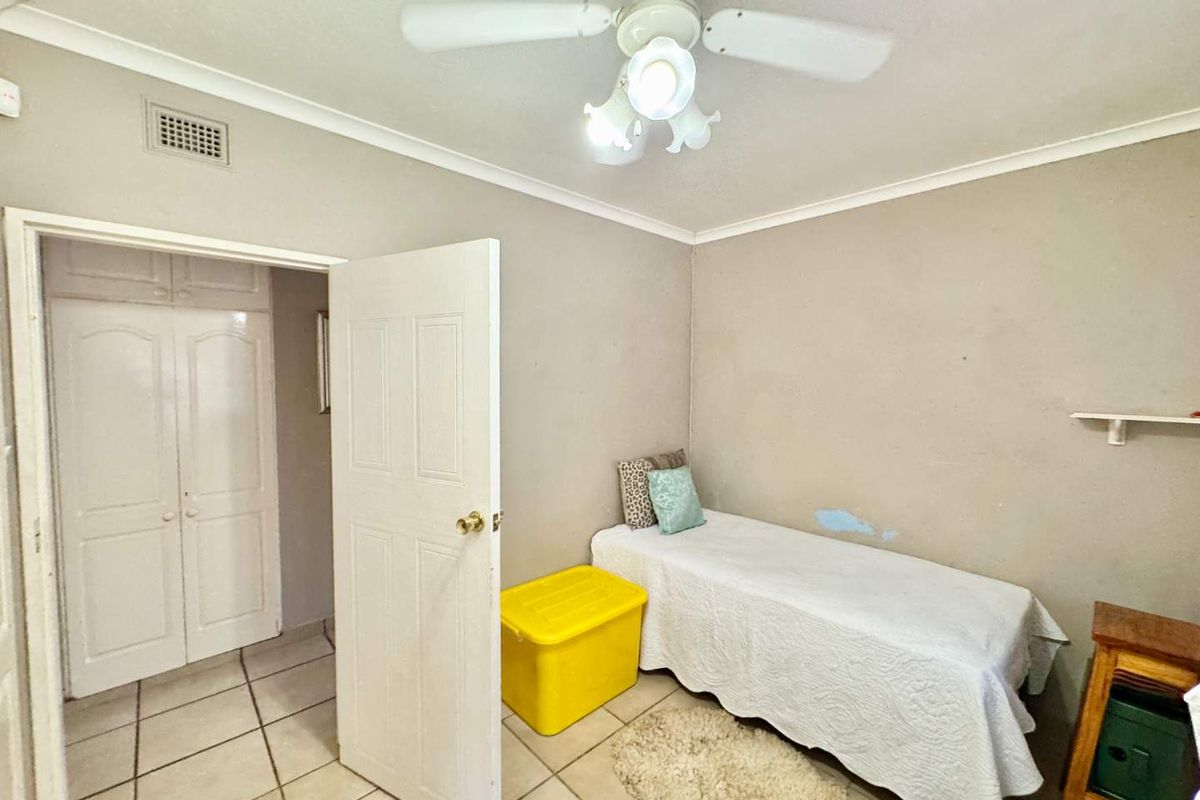 A bedroom featuring tiled flooring, built-in cupboards, and a ceiling fan, requiring minor cosmetic attention to the wall finishes.