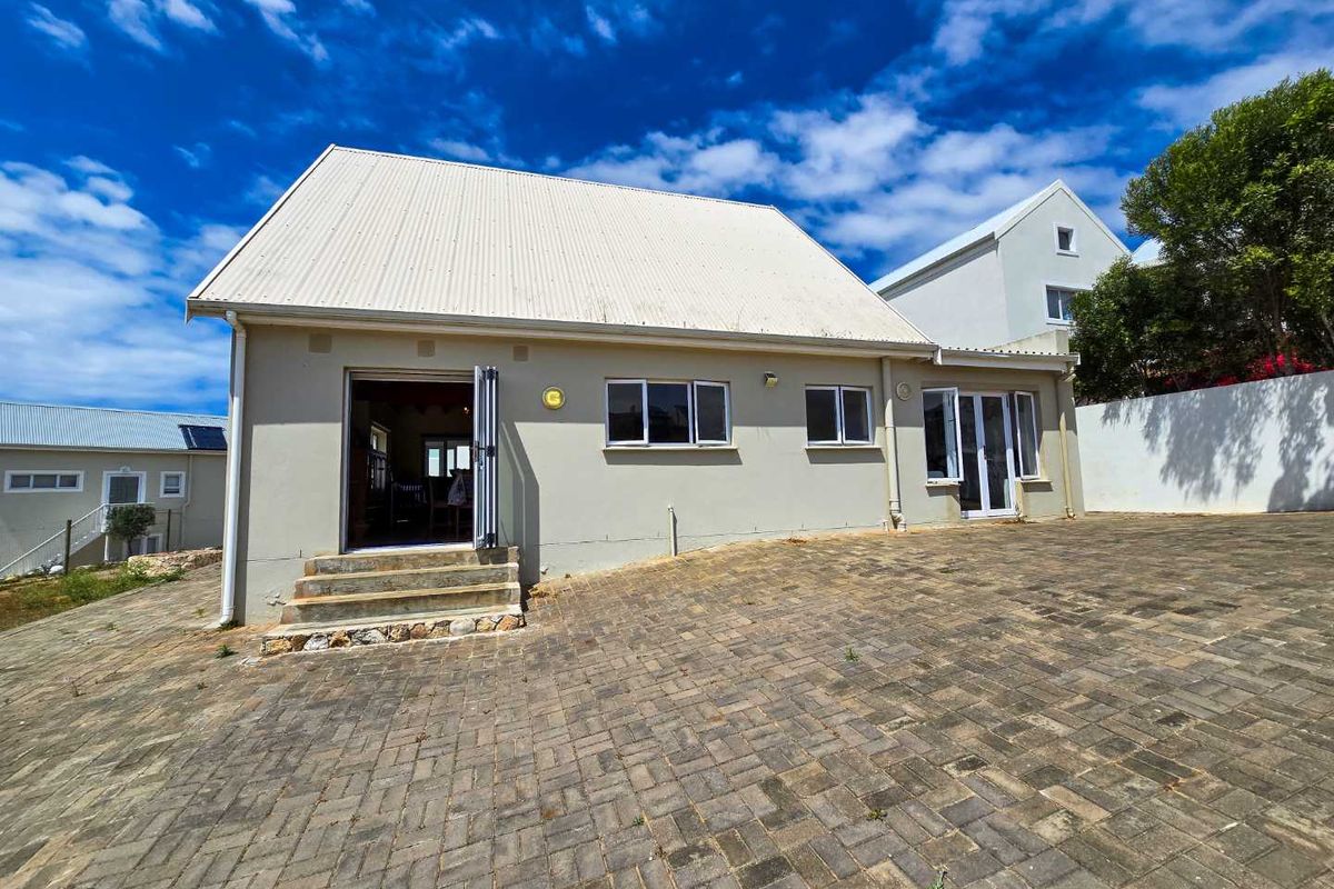 Rear view of the property featuring a paved courtyard, corrugated metal roof, and bi-fold door access to the interior living space.