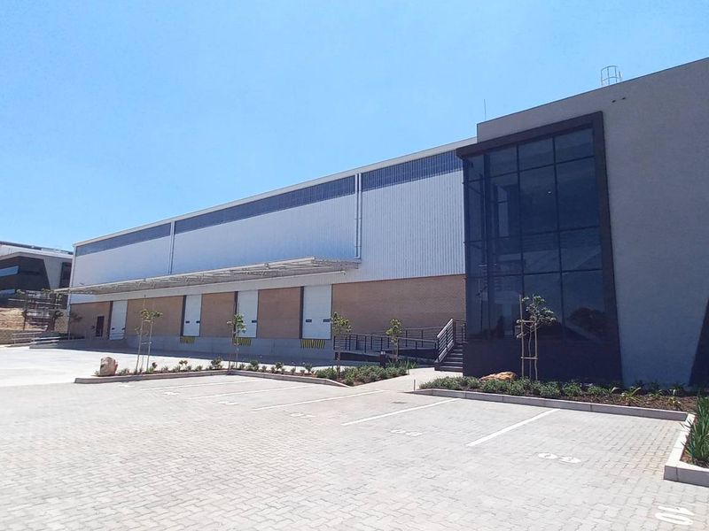 Modern industrial warehouse facility featuring multiple loading docks, extensive paved yard space, and contemporary architectural facade with large glass curtain wall elements.
