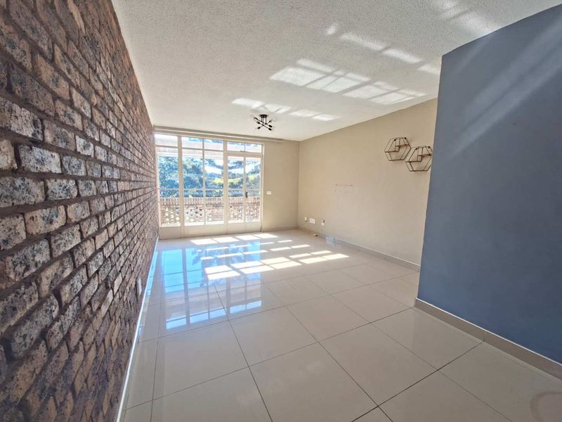 A bright, empty living room featuring a textured exposed brick wall, large glass sliding doors, and polished floor tiles.