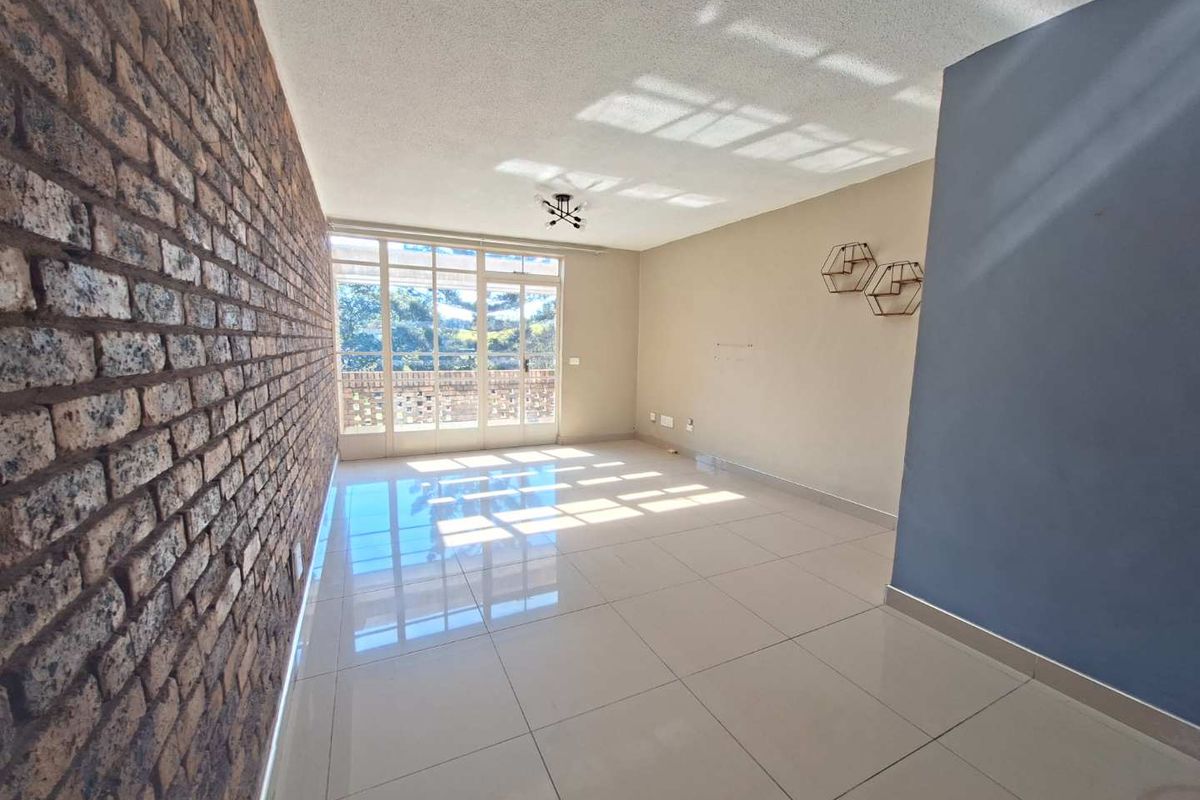 A bright, empty living room featuring a textured exposed brick wall, large glass sliding doors, and polished floor tiles.