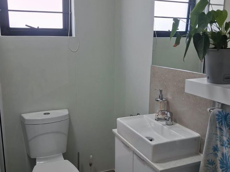 A clean and functional bathroom featuring a modern vanity with basin, toilet, and wall-mounted mirror, finished with neutral tiling.