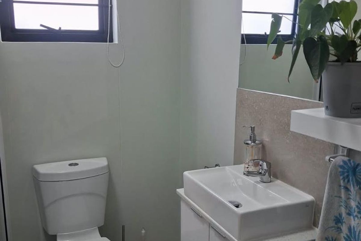 A clean and functional bathroom featuring a modern vanity with basin, toilet, and wall-mounted mirror, finished with neutral tiling.