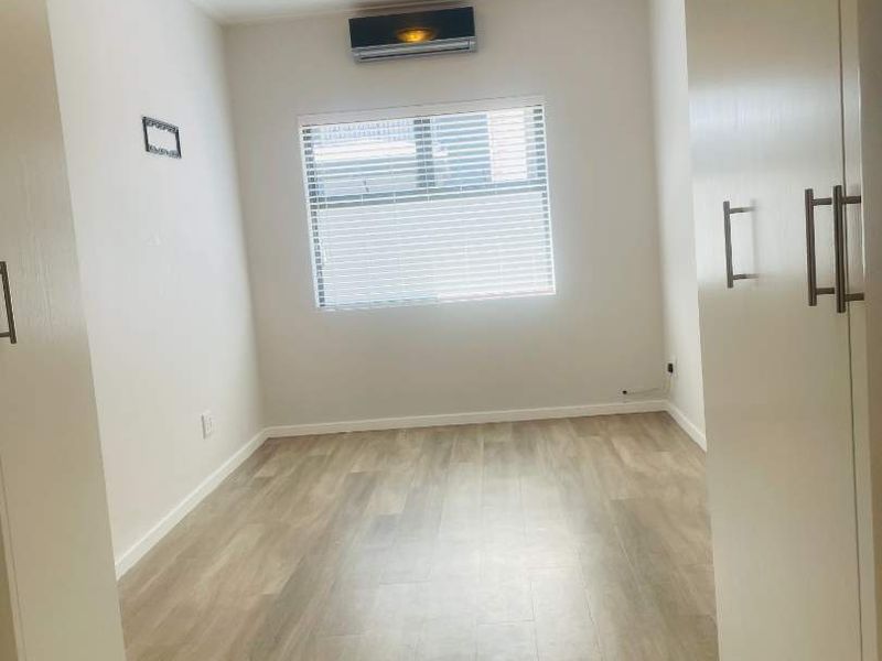 A bright, empty bedroom featuring modern laminate flooring, built-in cupboards, and a wall-mounted air conditioning unit.