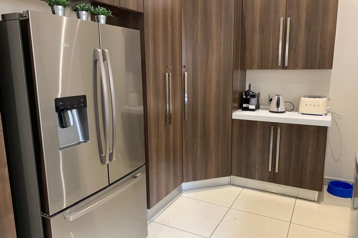 Modern kitchen area featuring dark wood cabinetry, white stone countertops, and large format floor tiles.