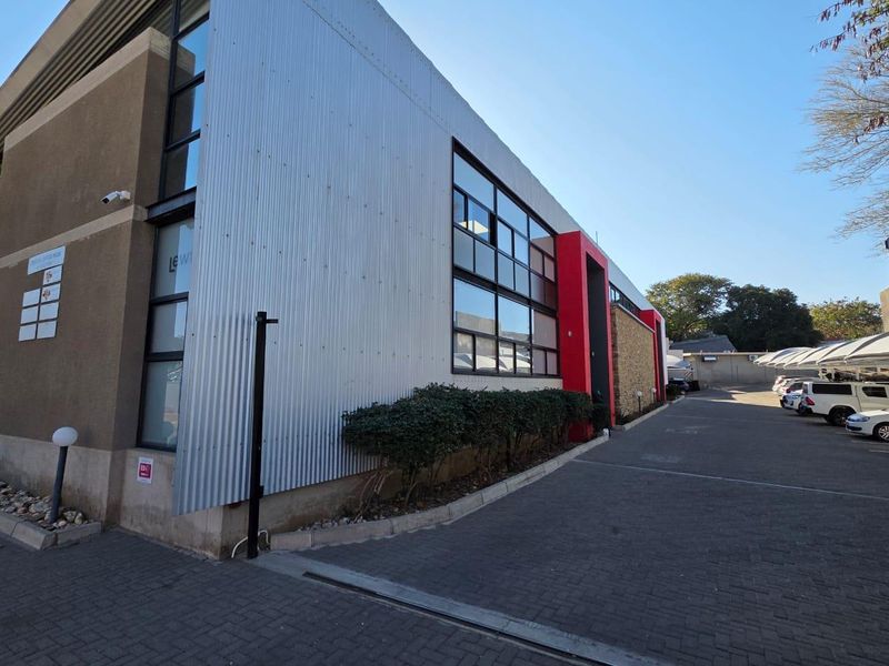 Modern office building exterior featuring corrugated metal cladding, large glass windows, and a paved driveway with ample parking space.