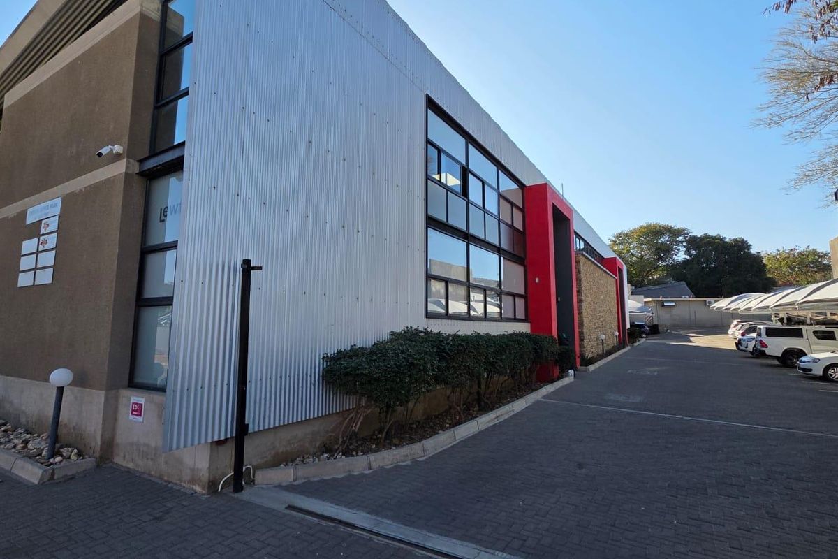Modern office building exterior featuring corrugated metal cladding, large glass windows, and a paved driveway with ample parking space.