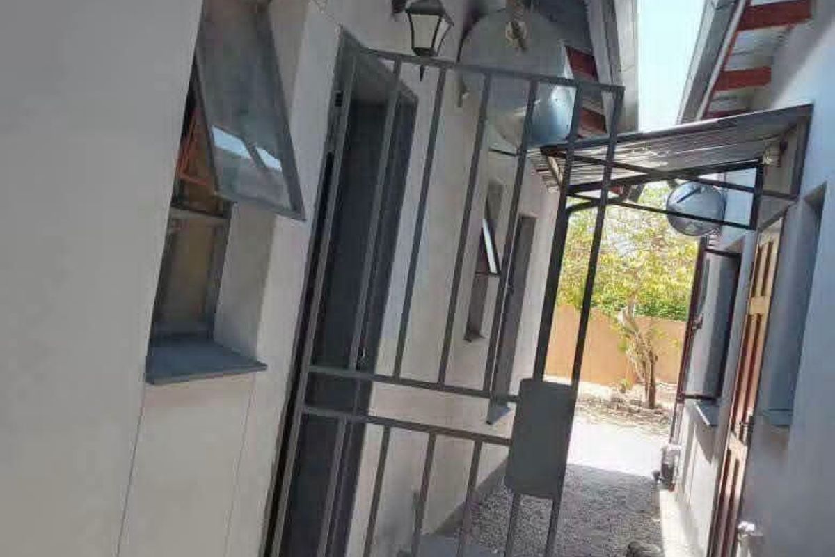 A narrow side passage of the house featuring a security gate, external lighting, and corrugated roofing over the walkway.