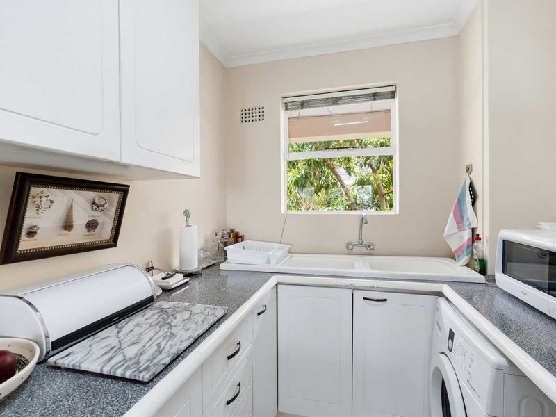 A functional laundry room featuring white built-in cabinetry, a double basin sink, and a laminate countertop with space for under-counter appliances.