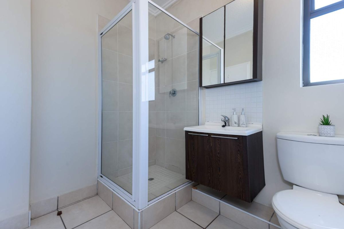 A functional bathroom featuring a glass-enclosed shower, a wall-mounted vanity with a mirror cabinet, and a standard toilet.