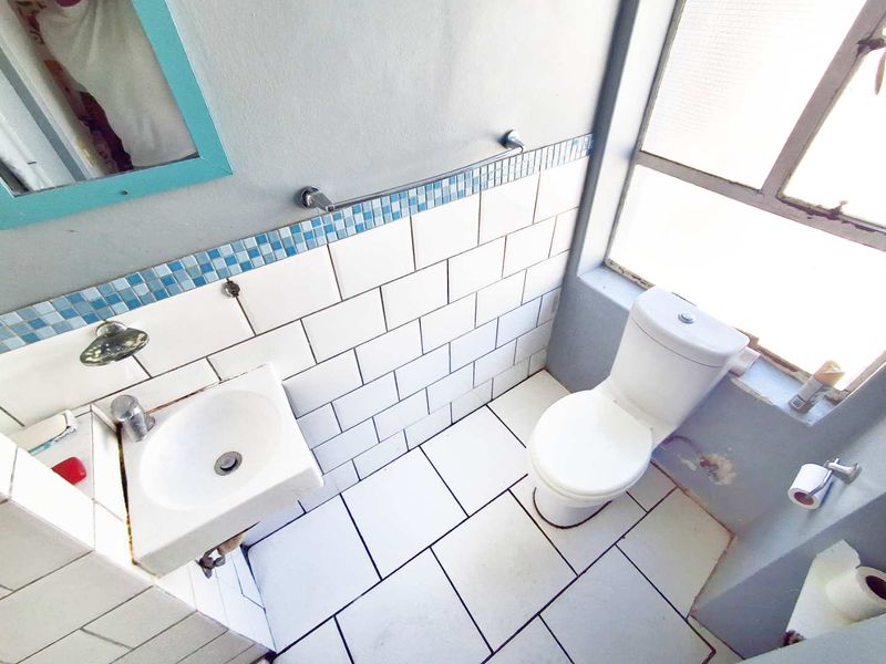A compact bathroom featuring a wall-mounted basin, toilet, and tiled splashback with a metal-framed window providing natural light.