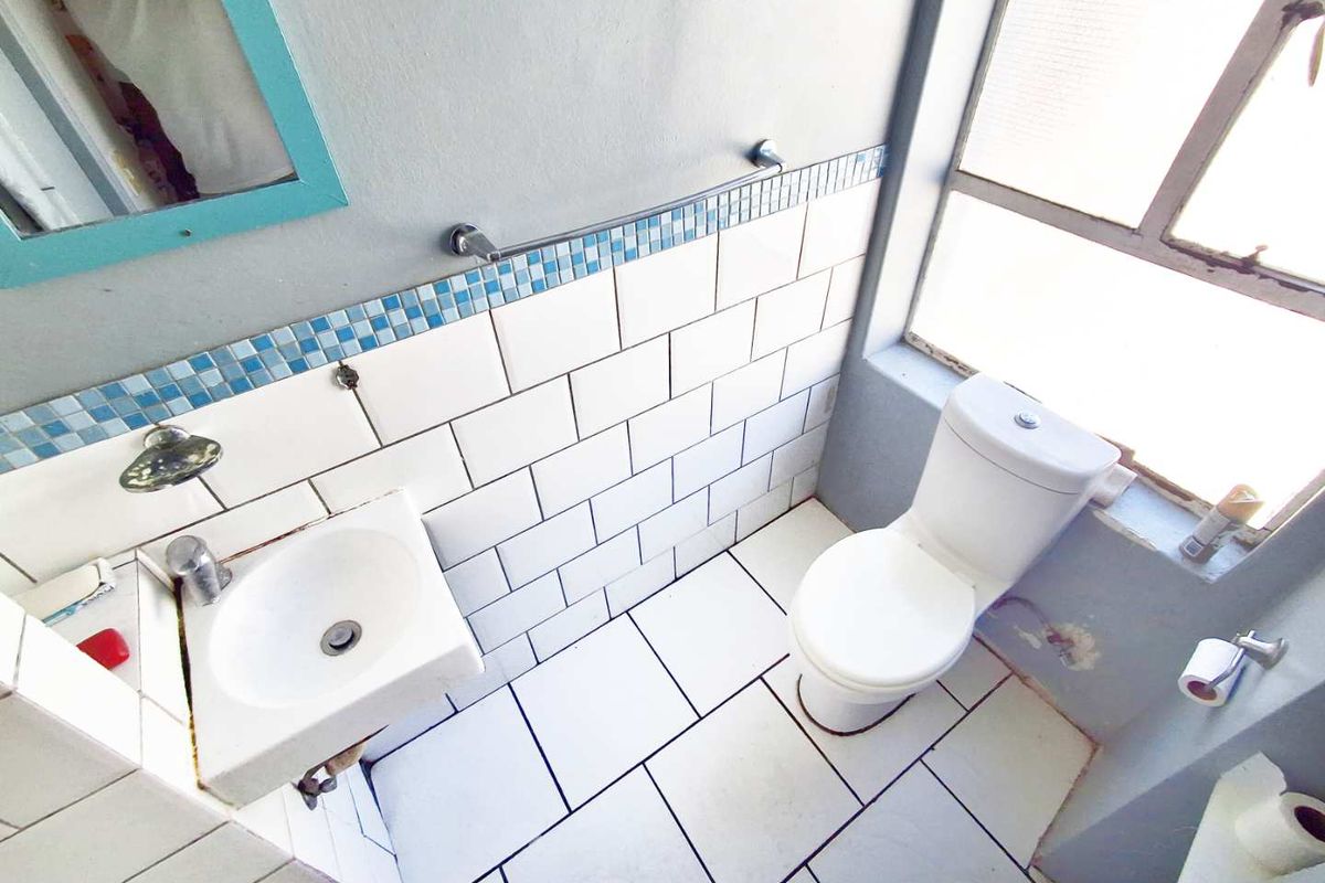 A compact bathroom featuring a wall-mounted basin, toilet, and tiled splashback with a metal-framed window providing natural light.