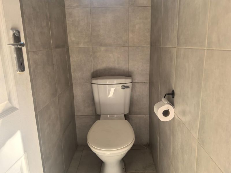 A compact, tiled guest toilet featuring neutral ceramic wall and floor tiles.