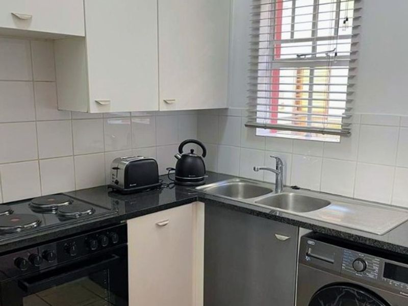 Compact kitchen featuring white cabinetry, dark countertops, tiled backsplash, built-in oven, electric hob, and integrated laundry appliance space.