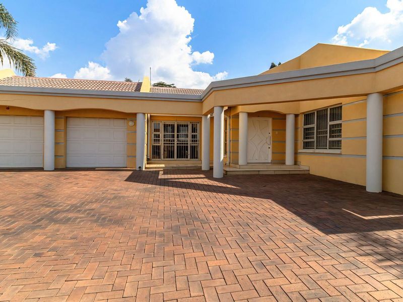 Front elevation of a house featuring a paved driveway, double garage, and a covered entrance with architectural columns.