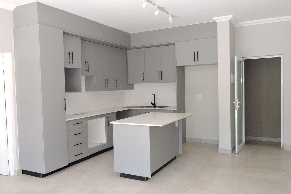 Modern kitchen featuring grey cabinetry, white stone countertops, a central island, subway tile backsplash, and sleek black fixtures in an open-plan layout.