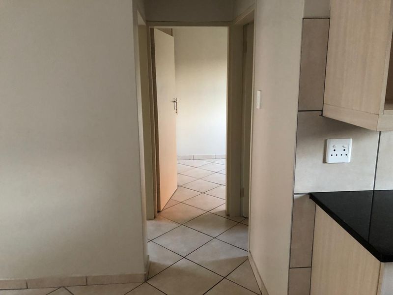 A neutral hallway featuring tiled flooring and access to adjacent rooms, with a glimpse of kitchen cabinetry and a doorway leading to a bedroom.