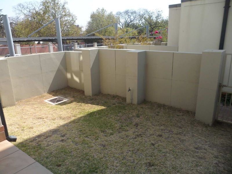 A private rear courtyard area featuring a small lawn, boundary walls, an external water tap, and a metal access gate.