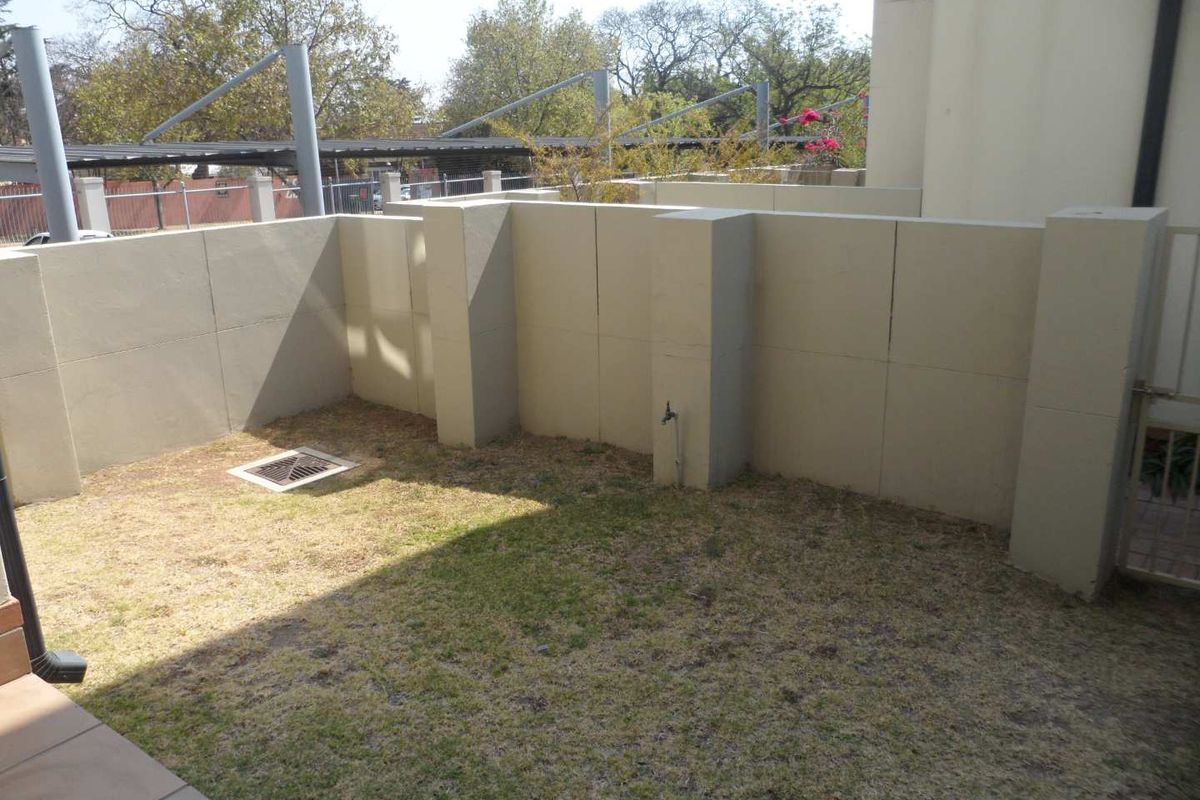 A private rear courtyard area featuring a small lawn, boundary walls, an external water tap, and a metal access gate.