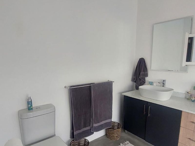 A modern bathroom featuring a dark vanity cabinet with a vessel sink, a wall-mounted mirror, and a standard toilet on concrete flooring.