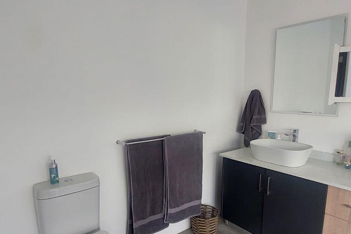 A modern bathroom featuring a dark vanity cabinet with a vessel sink, a wall-mounted mirror, and a standard toilet on concrete flooring.