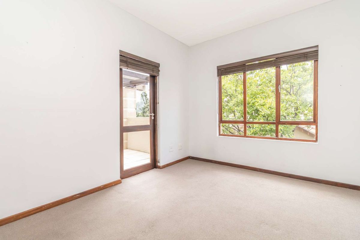An empty bedroom featuring neutral carpeting, large windows with wooden blinds, and a glass-paneled door providing access to an outdoor balcony area.