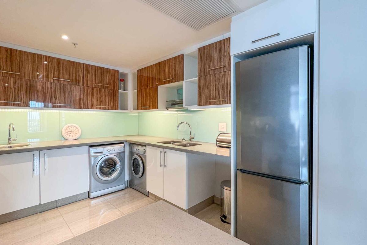 Modern kitchen featuring wood-grain cabinetry, light-colored countertops, a glass splashback, and integrated space for laundry appliances.