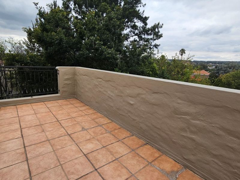 A spacious open-air balcony featuring tiled flooring, a solid masonry parapet wall, and a metal balustrade with elevated views of the surrounding area.