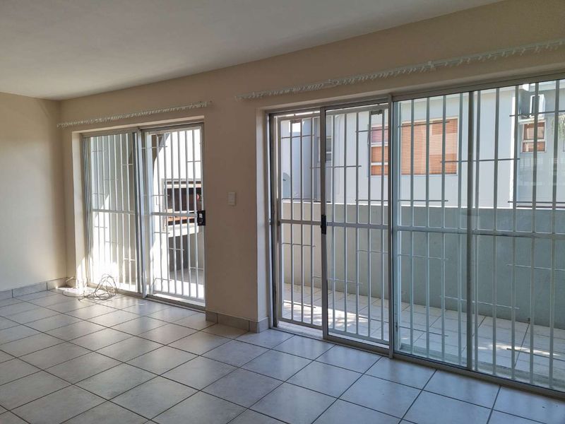 Spacious living area featuring ceramic floor tiles and dual sliding glass doors with security gates, providing direct access to an outdoor patio with built-in braai.