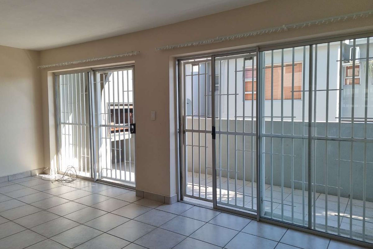 Spacious living area featuring ceramic floor tiles and dual sliding glass doors with security gates, providing direct access to an outdoor patio with built-in braai.