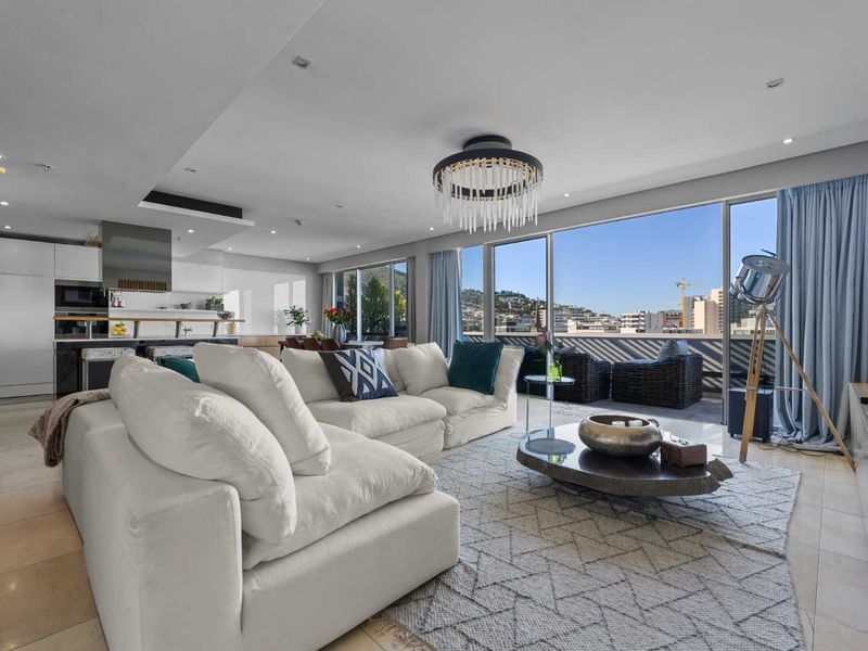 Spacious open-plan living area featuring modern kitchen cabinetry, stone flooring, and expansive floor-to-ceiling glass doors leading to a private balcony with city views.