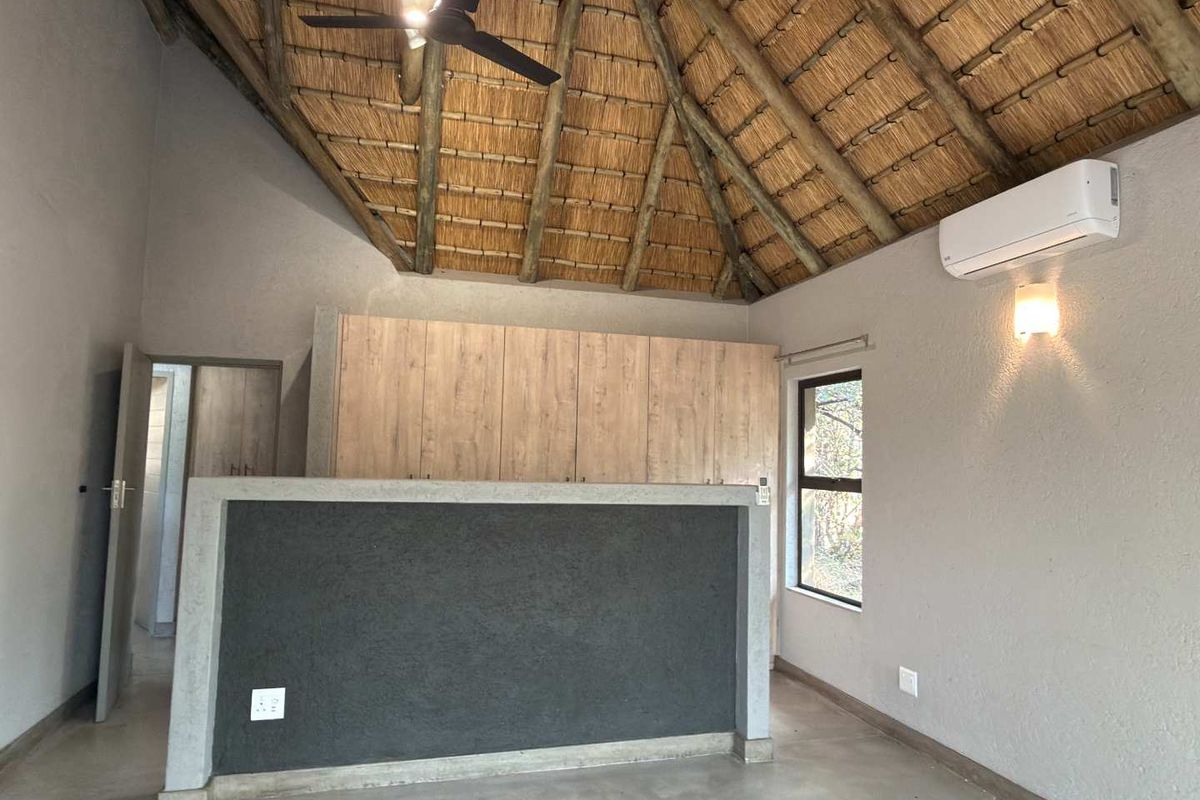 A modern bedroom featuring a high vaulted thatched ceiling, polished concrete flooring, built-in cabinetry, and a wall-mounted air conditioning unit.