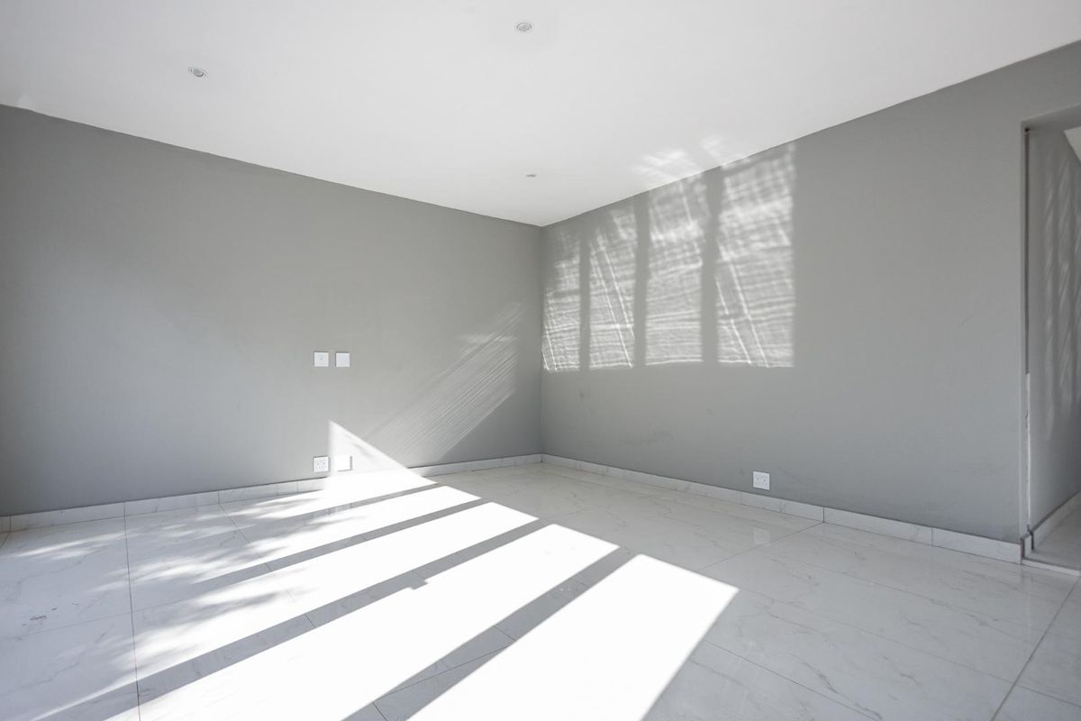 A bright, empty living room featuring neutral grey walls, white tiled flooring, and recessed ceiling lighting.