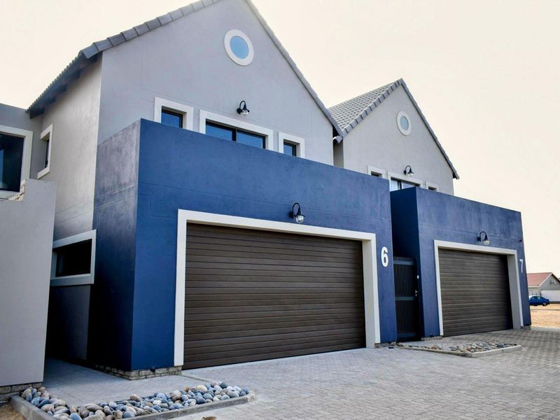 Modern townhouse exterior featuring a double garage with sectional doors, paved driveway, and contemporary blue and grey facade finishes.