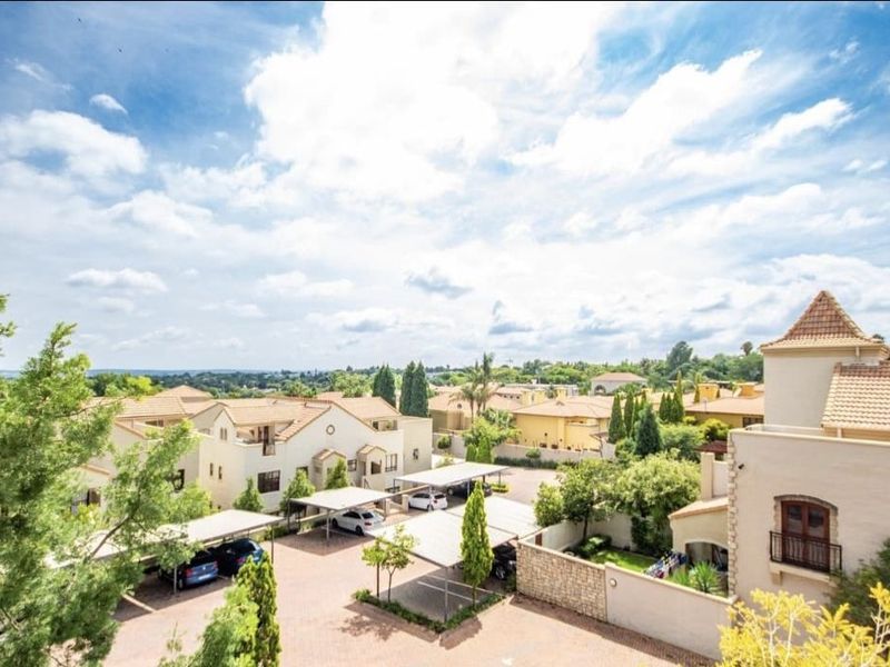 An elevated aerial view of a residential apartment complex featuring paved driveways, covered parking carports, and landscaped grounds under a bright sky.