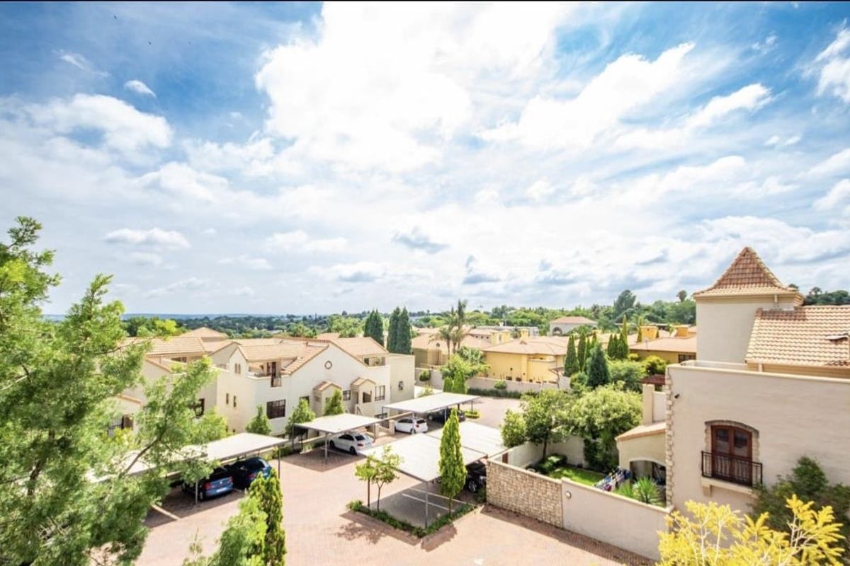 An elevated aerial view of a residential apartment complex featuring paved driveways, covered parking carports, and landscaped grounds under a bright sky.