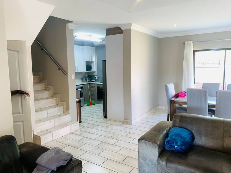 Open plan living and dining area featuring tiled flooring, a staircase with a metal handrail, and direct access to a kitchen with built-in cabinetry.
