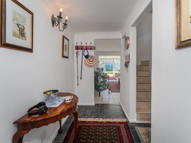 A bright entrance hallway featuring tiled flooring, coving, and a staircase leading to the upper level, with a view through to the living area.