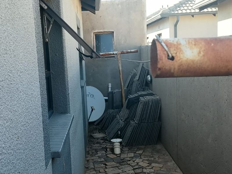 A narrow side passage of the property featuring paved flooring, plastered boundary walls, and visible exterior plumbing fixtures.