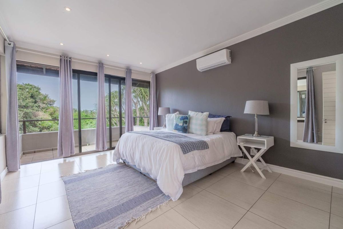 Spacious bedroom featuring large sliding glass doors leading to a private balcony, tiled flooring, and a wall-mounted air conditioning unit.