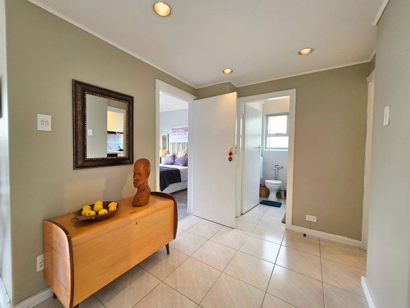 A well-lit hallway featuring neutral wall tones and tiled flooring, providing access to the bedroom and bathroom areas.