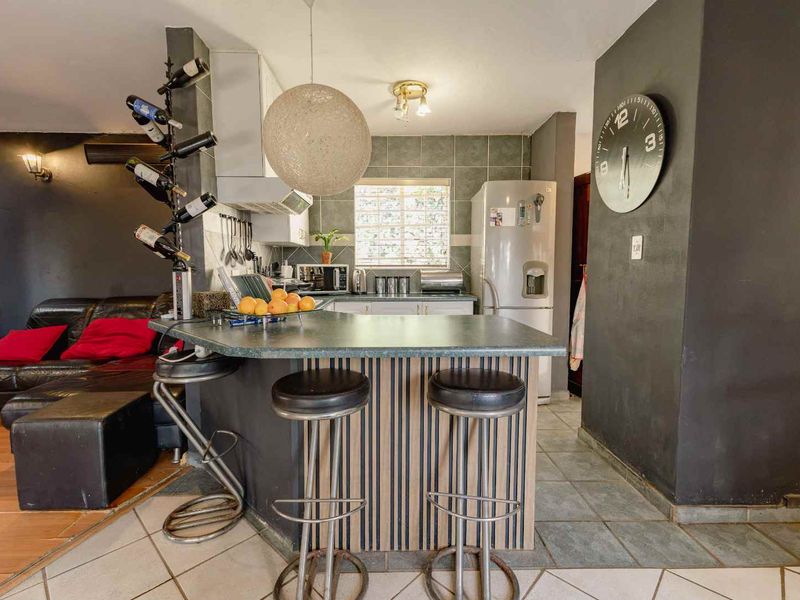 Open-plan kitchen and living area featuring a breakfast bar, tiled flooring, and functional cabinetry, creating a connected space for cooking and relaxation.